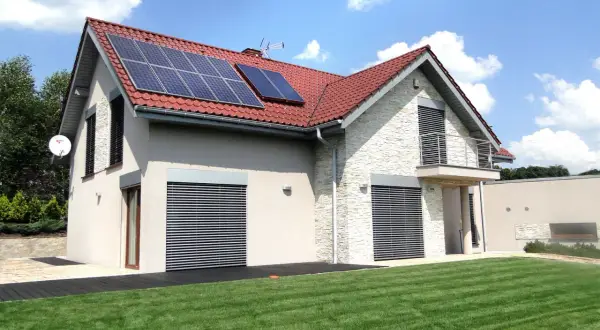 Nowoczesny dom z panelami solarnymi na dachu, otoczony zielonym ogrodem.