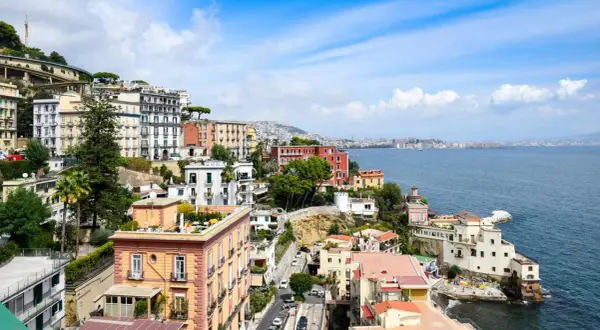 Färgstarka hus klättrar uppför sluttningen vid Neapel, Italien, med havet glittrande i bakgrunden.