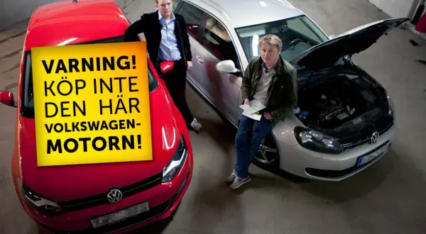 Två män står vid bilar. En röd bil har en gul skylt med texten "VARNING! KÖP INTE DEN HÄR VOLKSWAGEN-MOTORN!". En silverfärgad bil har motorhuven öppen.