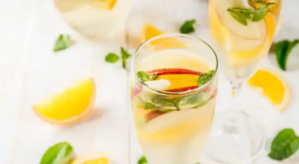 Verre de sangria blanche garni de tranches de pomme, d'orange et de menthe fraîche. Parfait pour une journée ensoleillée.