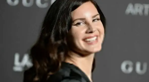 Uśmiechnięta Lana Del Rey, artystka znana z nastrojowych piosenek, na tle logo Gucci.