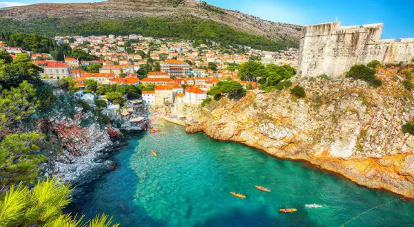Kajaker på tur i det turkosa vattnet vid Gamla stan Dubrovnik, med klippor och stadens takåsar i bakgrunden.