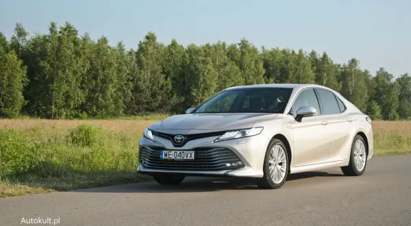 Elegancka Toyota Camry 2025 w kolorze szampańskim na tle zielonego krajobrazu.