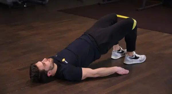 Mężczyzna wykonuje ćwiczenie glute bridge z gumą na udach, napinając pośladki.