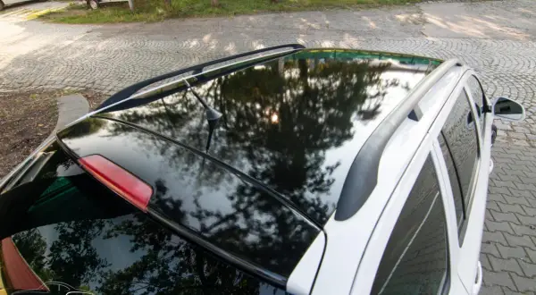 Błyszczące oklejenie dachu samochodu odbija drzewa i słońce. Eleganckie wykończenie dodaje autu stylu.
