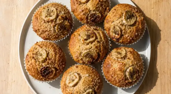 Sju gyllene bananmuffins med skivor av banan på toppen, redo att avnjutas. Ett perfekt bananmuffins recept!