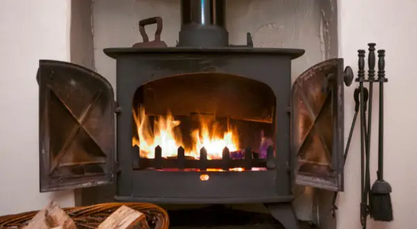 Ein Holzofen mit brennendem Feuer. Daneben ein Korb mit **Holz** und ein Werkzeugset. Die **Asche** glüht im Feuer.