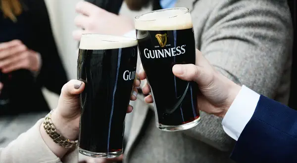 Dwie osoby wznoszą toast szklankami ciemnego piwa Guinness. To klasyczne piwo ma ok. 4,2% alkoholu.
