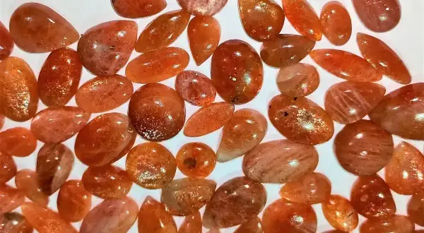 Mnóstwo błyszczących kamieni słonecznych o ciepłych, pomarańczowych odcieniach, ułożonych na białym tle.