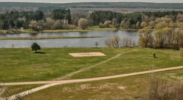Łąka z boiskiem do siatkówki plażowej i rzeką w tle. W oddali las. Mielnik atrakcje przyrodnicze.