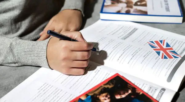Osoba pisze w zeszycie z flagą Wielkiej Brytanii. Uczy się angielskiego, a akronim co to?