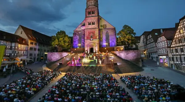 Bühnenaufführung vor historischer Kulisse in Hohenlohe. Ein großes Publikum verfolgt gespannt die Darbietung auf illuminierten Treppen vor einer Kirche.