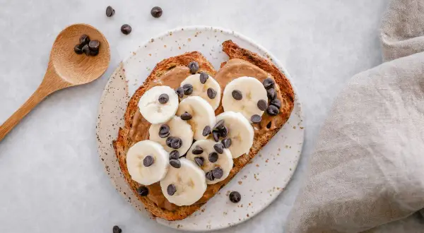 Tostada con mantequilla de maní, plátano en rodajas y chispas de chocolate. ¡Perfecta para merendar!