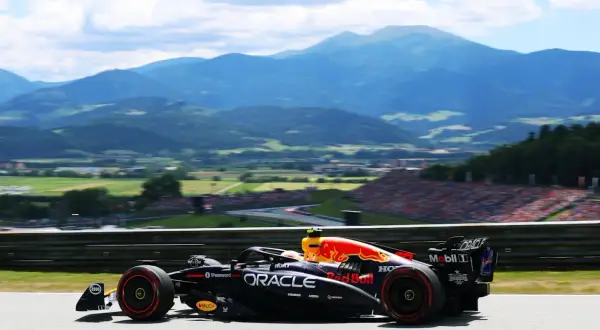 Un coche de Red Bull compite en el Gran Premio de Austria, con montañas y público al fondo.
