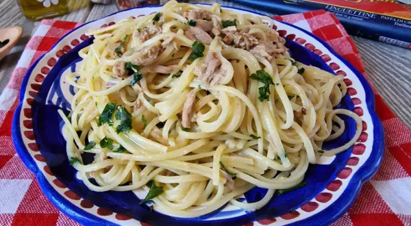 Un piatto di linguine con tonno e prezzemolo, condito con olio e peperoncino. Un classico della pasta al tonno in bianco, pronto per essere gustato.