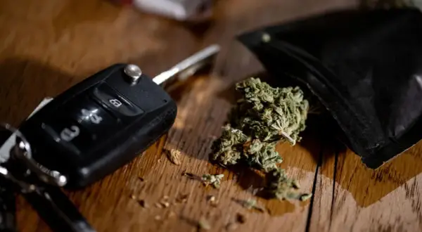 Autoschlüssel und Cannabis auf Holztisch. Ein gefährlicher Gedanke: Cannabis am Steuer.