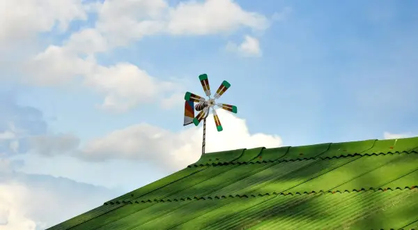 Piccolo impianto eolico domestico su tetto verde, con pale colorate che girano nel cielo azzurro con nuvole bianche.