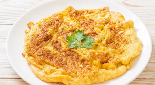 Złocisty omlet na talerzu, idealny jako omlet dla niemowlaka. Delikatny, puszysty, z gałązką pietruszki.