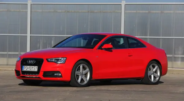 Czerwone Audi S5 z 2014 roku, sportowe coupe z elegancką linią, zaparkowane przed nowoczesnym budynkiem.