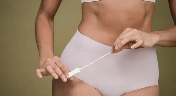 Kobieta trzymająca tampon, symbolizująca objawy miesiączki bez krwawienia.
