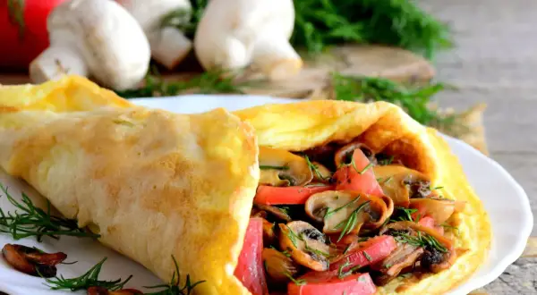 Puszysty omlet z pieczarkami i pomidorami, udekorowany koperkiem. Idealny na śniadanie.