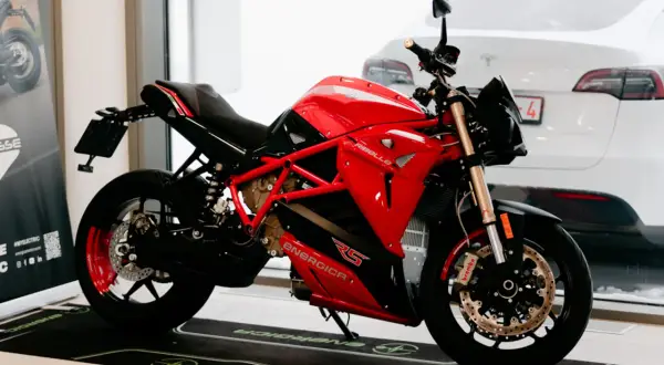 Motocicleta roja y negra Energica RS, lista para la acción. Detrás, un coche blanco.