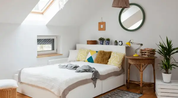 Chambre sous pente lumineuse avec lit blanc, coussins géométriques, et un puits de lumière. Une belle idée peinture pour un espace cosy.