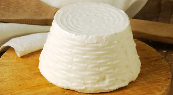 Świeży serek ricotta o stożkowatym kształcie, z charakterystycznym wzorem na wierzchu, leży na drewnianej desce.