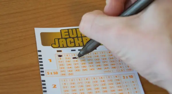 Ręka zaznacza liczby na kuponie Eurojackpot. Czy można grać w Eurojackpot mieszkając w Polsce, ale kupując los w Niemczech?