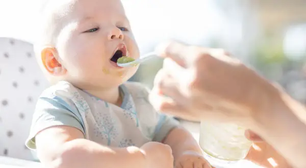 Niemowlę karmione mlekiem modyfikowanym otwiera buzię na łyżeczkę z zielonym puree. Czas zacząć rozszerzać dietę!