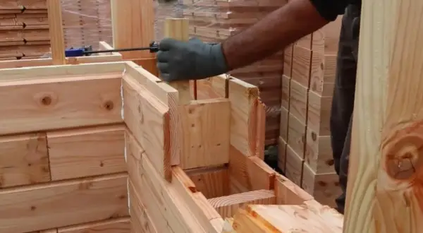 Construcción de una cabaña con madera aislante térmico. Un trabajador martilla una pieza de madera para encajarla.