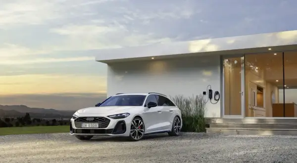 Białe Audi A6 Avant TFSI, zaparkowane przed nowoczesnym domem z ładowarką.