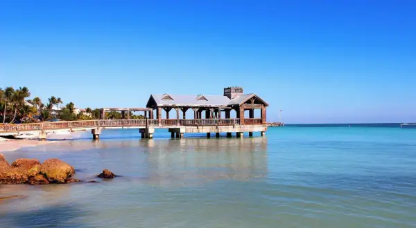 Un ponton en bois avec un kiosque, typique du parc Key West, s'avance sur une mer turquoise sous un ciel bleu éclatant.
