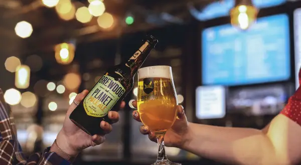 Brindisi con birra BrewDog Planet Pale Ale, perfetta per la Italy Beer Week. Luci soffuse e atmosfera da pub.