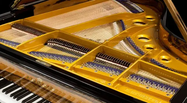 Wnętrze fortepianu, z widocznymi strunami i mechanizmem młoteczkowym. Złota płyta rezonansowa i drewniane wykończenie nadają mu elegancki wygląd. To piękny klawesyn.