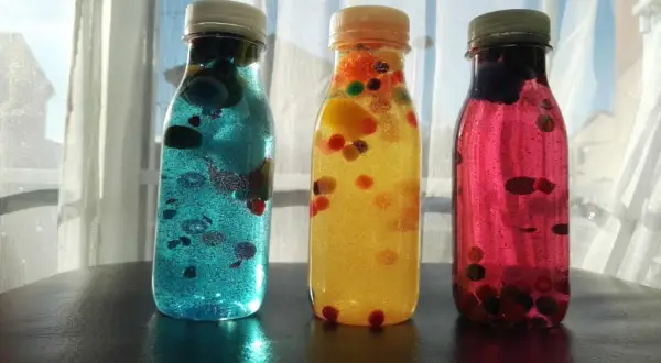 Tres botellas sensoriales caseras llenas de líquido brillante y bolitas de colores.