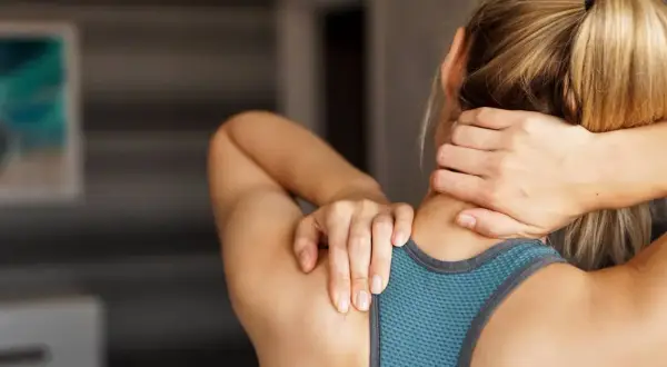 Une femme se masse le cou, peut-être pour soulager une douleur ou pour muscler son cou après un entraînement.