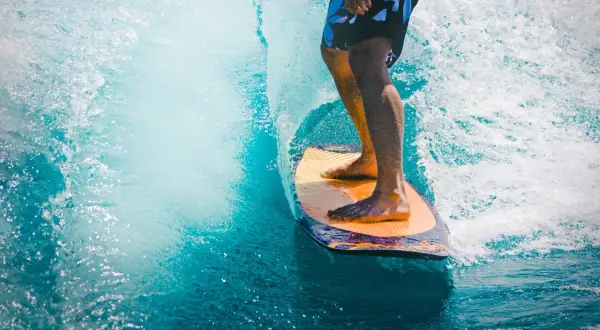 Mężczyzna na desce surfingowej, czując orzeźwienie wody, jak po użyciu perfum allure homme sport.