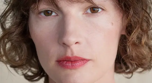Zbliżenie na twarz kobiety z brązowymi oczami i falowanymi włosami. Retinol dla kogo? Dla każdej kobiety pragnącej odmłodzonej skóry.