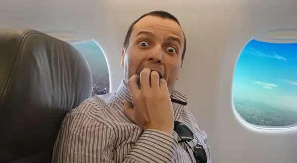Nerwowe pierwsze lot samolotem odczucia. Mężczyzna w pociągłym pasem, z szeroko otwartymi oczami, gryzie paznokcie, patrząc w okno samolotu.