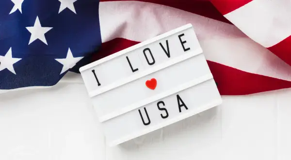 Amerykańska flaga i tablica z napisem "I LOVE USA". Zastanawiasz się, ile kosztuje bilet do USA w dwie strony?
