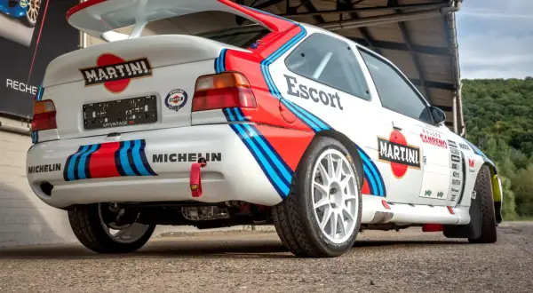 Biały Ford Escort Cosworth w barwach Martini Racing, z dużym tylnym spojlerem i licznymi naklejkami sponsorów.