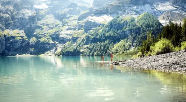 Zwei Personen genießen die Erfrischung in einem türkisfarbenen See vor majestätischen Schweizer Alpen.