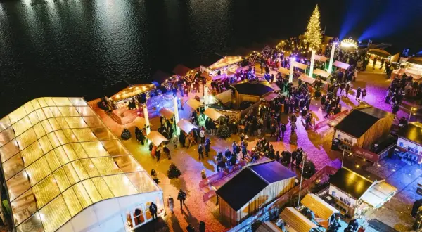 Buntes Treiben auf einem weihnachtsmarkt an der Spree. Menschen schlendern zwischen beleuchteten Buden und einem großen Weihnachtsbaum.