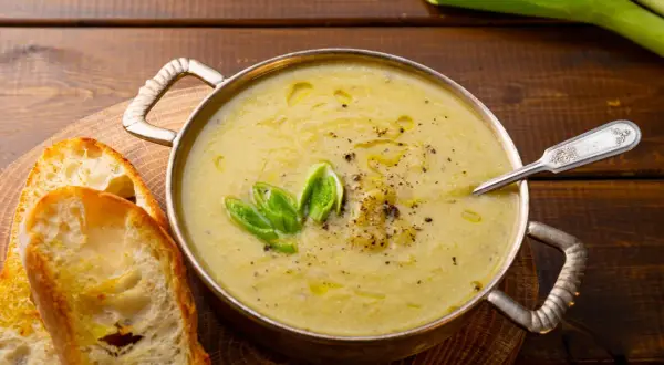 Una ciotola di calda crema di patate, guarnita con cipollotto fresco e pepe nero, servita con fette di pane tostato.