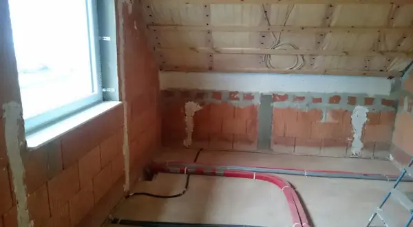 Neue Heizungsrohre verlegen im Rohbau. Rote und graue Rohre liegen auf dem Boden, bereit für die Installation.
