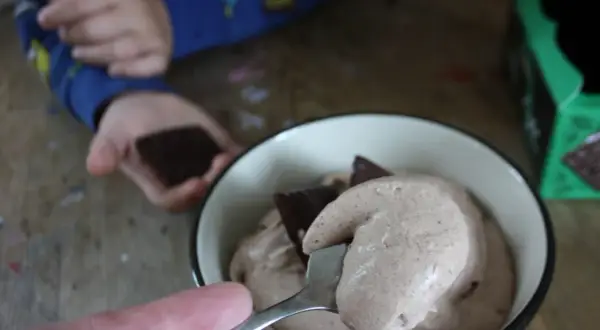 En sked med krämig after eight mousse lyfts ur en skål. En barnhand håller en chokladbit i bakgrunden.