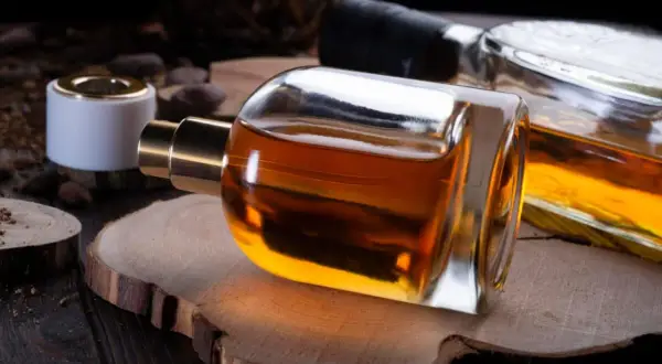 Elegancka butelka perfum o bursztynowym kolorze, sugerująca nuty wanilii i tytoniu, leży na drewnianym plastrze.