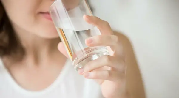 Kobieta pije wodę z filtra, która ma gorzki smak.