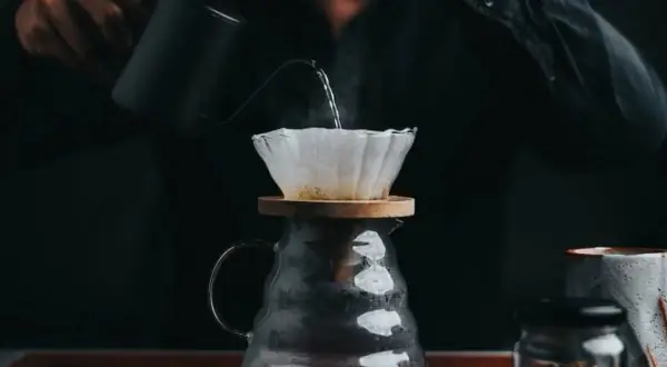 En person häller varmt vatten över kaffefilter för att brygga dropp kaffe. Ånga stiger från den nybryggda drycken.